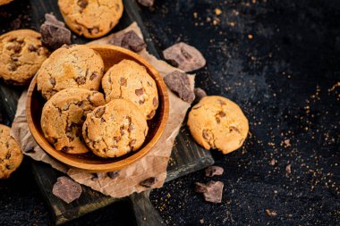 Cookies with pieces of milk chocolate on a cutting board. On a black background. High quality photo