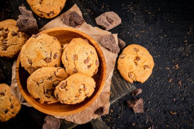 Cookies with pieces of milk chocolate on a cutting board. On a black background. High quality photo