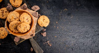 Cookies with pieces of milk chocolate on a cutting board. On a black background. High quality photo