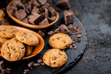 Cookies with pieces of milk chocolate on a stone board. On a black background. High quality photo