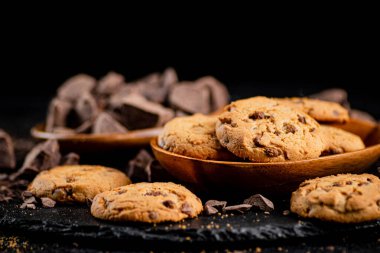 Cookies with pieces of milk chocolate on a stone board. On a black background. High quality photo