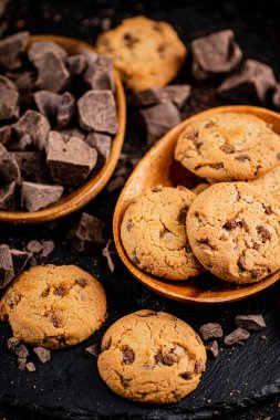 Cookies with pieces of milk chocolate on a stone board. On a black background. High quality photo