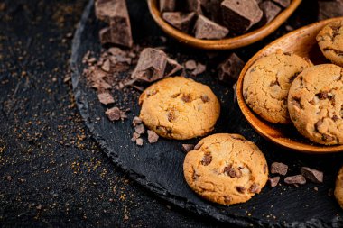 Cookies with pieces of milk chocolate on a stone board. On a black background. High quality photo