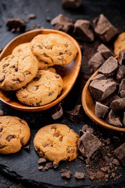 Cookies with pieces of milk chocolate on a stone board. On a black background. High quality photo