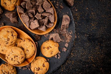 Cookies with pieces of milk chocolate on a stone board. On a black background. High quality photo