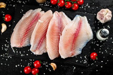 Raw fish fillet with spices and tomatoes on a stone board. On a black background. High quality photo