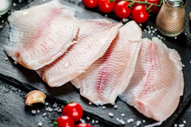 Raw fish fillet with spices and tomatoes on a stone board. On a black background. High quality photo