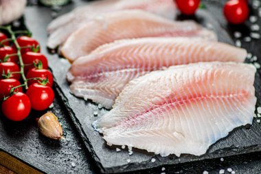 Raw fish fillet with spices and tomatoes on a stone board. On a black background. High quality photo