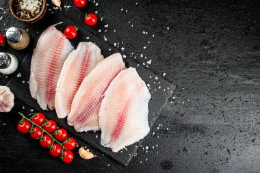 Raw fish fillet with spices and tomatoes on a stone board. On a black background. High quality photo