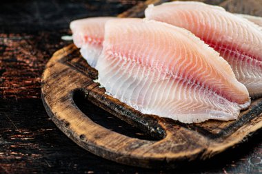 Raw fish fillet on a wooden cutting board. Against a dark background. High quality photo