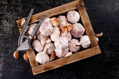 Garlic on a wooden tray with a garlic press. On a black background. High quality photo