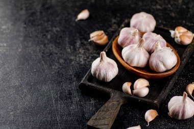 Garlic on a wooden plate on a cutting board. On a black background. High quality photo