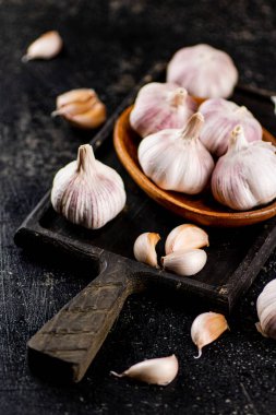 Garlic on a wooden plate on a cutting board. On a black background. High quality photo