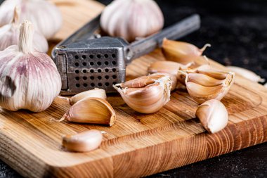 Cloves of garlic on a cutting board with a garlic press. On a black background. High quality photo