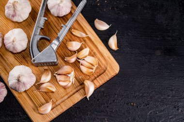 Cloves of garlic on a cutting board with a garlic press. On a black background. High quality photo