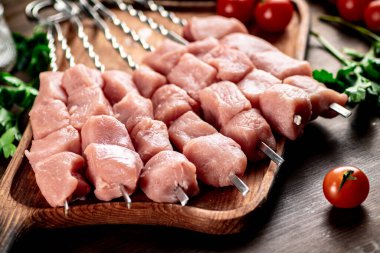 Pork kebab raw on skewers with parsley and tomatoes on a cutting board. On a wooden background. High quality photo