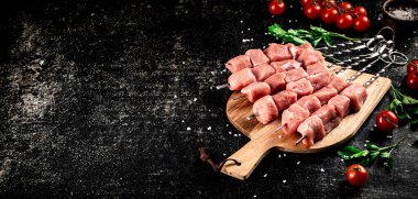 Pork kebab raw on a cutting board with tomatoes and parsley. On a black background. High quality photo