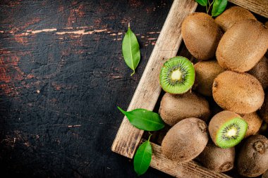 Fragrant kiwi with leaves on tray. On a rustic dark background. High quality photo