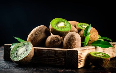 Fragrant kiwi with leaves on tray. On a rustic dark background. High quality photo