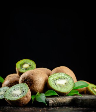 A pile of kiwi with leaves on a cutting board. On a black background. High quality photo