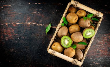Fresh kiwi with leaves in a basket. On a rustic dark background. High quality photo