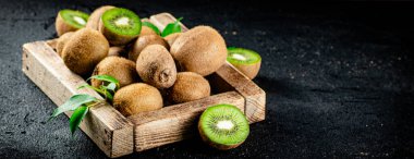 Ripe kiwi with leaves on a wooden tray. On a black background. High quality photo