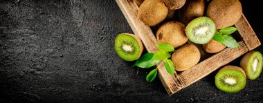 Ripe kiwi with leaves on a wooden tray. On a black background. High quality photo