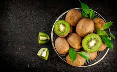 Ripe kiwi with leaves in a colander on the table. On a black background. High quality photo