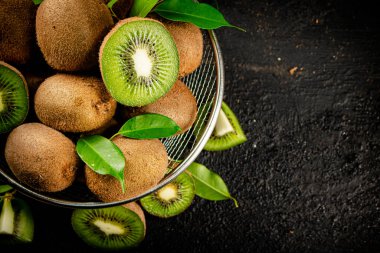 Ripe kiwi with leaves in a colander on the table. On a black background. High quality photo