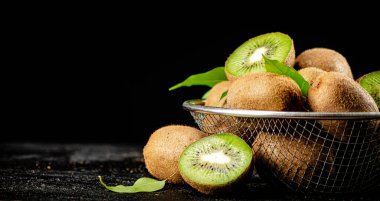 Ripe kiwi with leaves in a colander on the table. On a black background. High quality photo