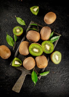 Pieces of kiwi with leaves on a cutting board. On a black background. High quality photo