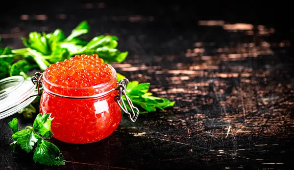 stock image A full jar of red caviar with parsley on the table. On a rustic dark background. High quality photo