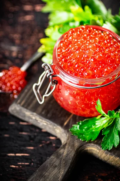 stock image A full glass jar of red caviar on a cutting board. Against a dark background. High quality photo