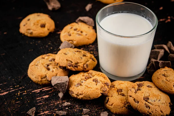 Homemade cookies with pieces of milk chocolate and a glass of milk. Against a dark background. High quality photo