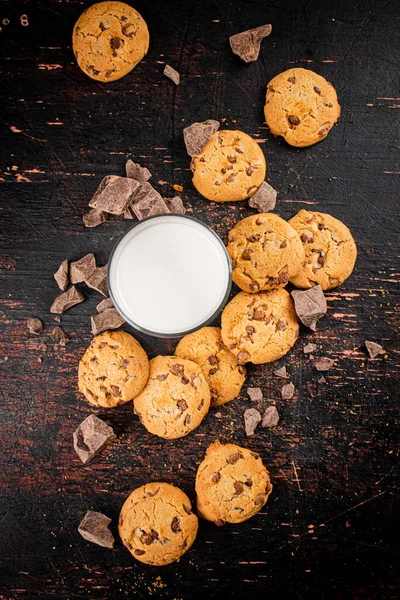 Homemade cookies with pieces of milk chocolate and a glass of milk. Against a dark background. High quality photo