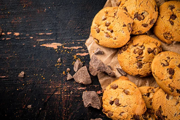 Cookies with pieces of milk chocolate on the table. On a rustic dark background. High quality photo