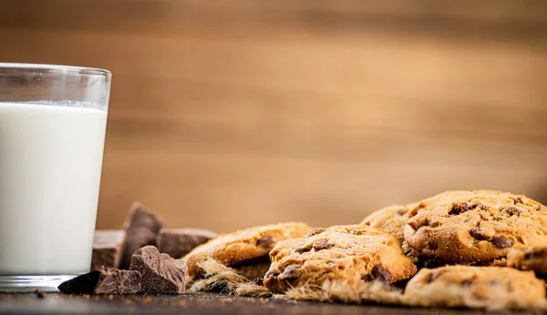 Cookies with pieces of milk chocolate with a glass of milk. On a wooden background. High quality photo
