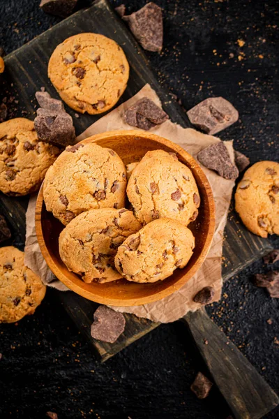 Cookies with pieces of milk chocolate on a cutting board. On a black background. High quality photo