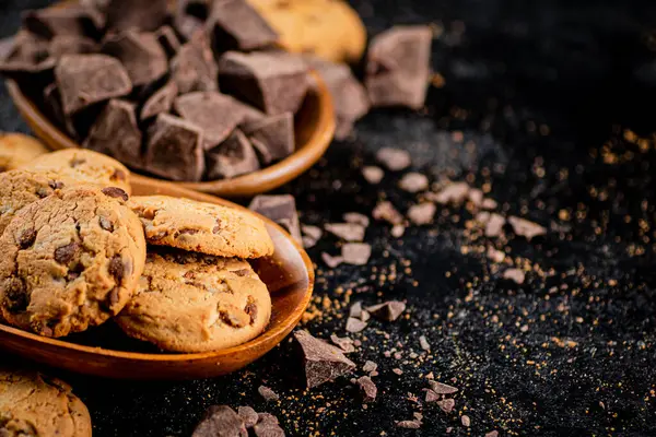 Wooden plate with cookies and pieces of milk chocolate. On a black background. High quality photo