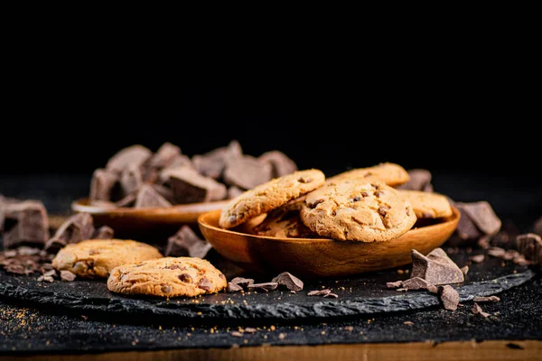 Cookies with pieces of milk chocolate on a stone board. On a black background. High quality photo