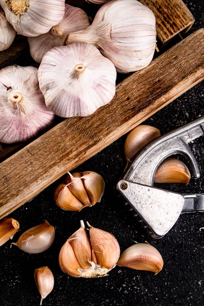 Garlic on a wooden tray with a garlic press. On a black background. High quality photo