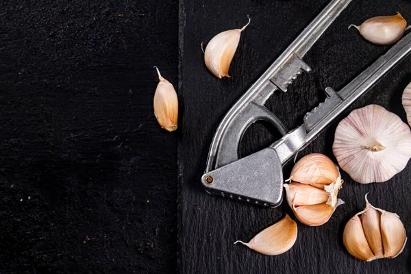 Garlic with a garlic press on a stone board. On a black background. High quality photo