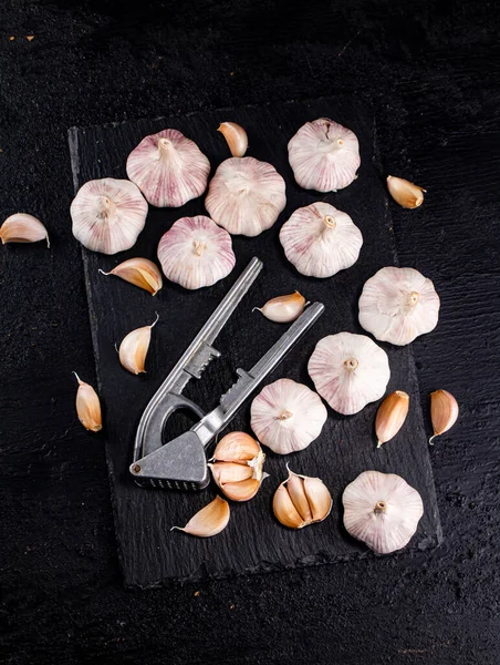 Garlic with a garlic press on a stone board. On a black background. High quality photo