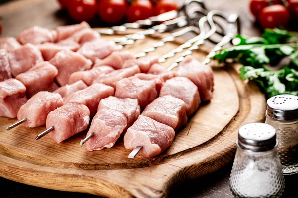 Pork kebab raw on skewers with parsley and tomatoes on a cutting board. On a wooden background. High quality photo