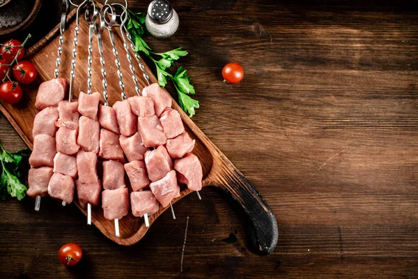 Pork kebab raw on skewers with parsley and tomatoes on a cutting board. On a wooden background. High quality photo