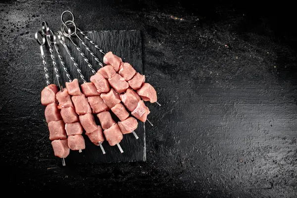 Pork kebab raw on skewers on a stone board. On a black background. High quality photo