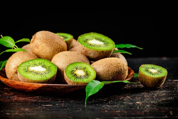 Fresh kiwi with leaves on a wooden plate. Against a dark background. High quality photo