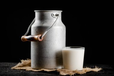 Rustic milk in a can and a glass on the table. On a black background. High quality photo