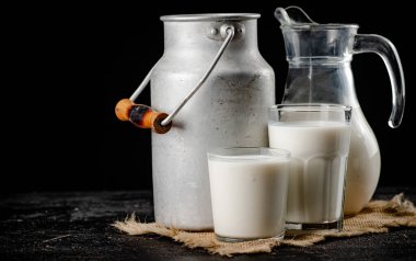 Rustic milk in a can and a glass on the table. On a black background. High quality photo
