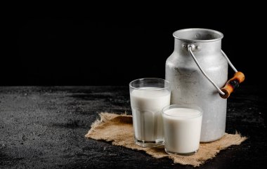 Rustic milk in a can and a glass on the table. On a black background. High quality photo